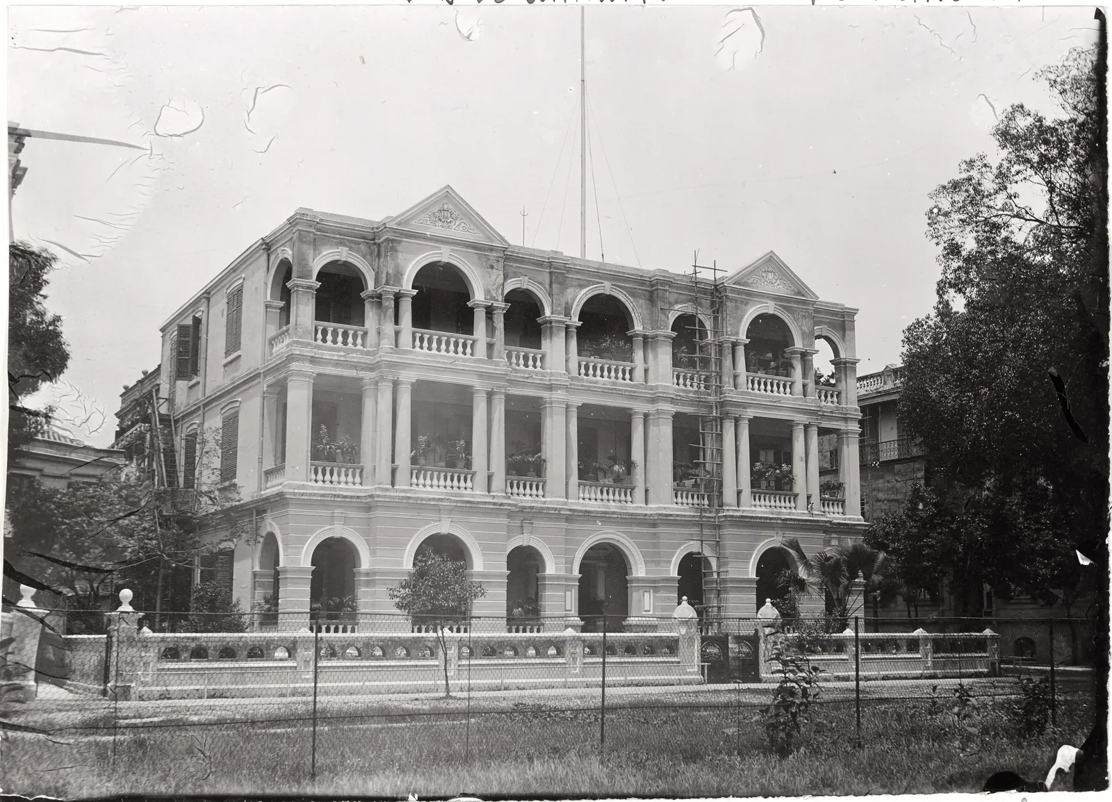 A three-storey rendered building with arcaded verandahs on every floor and two pediments, behind a balustraded wall.