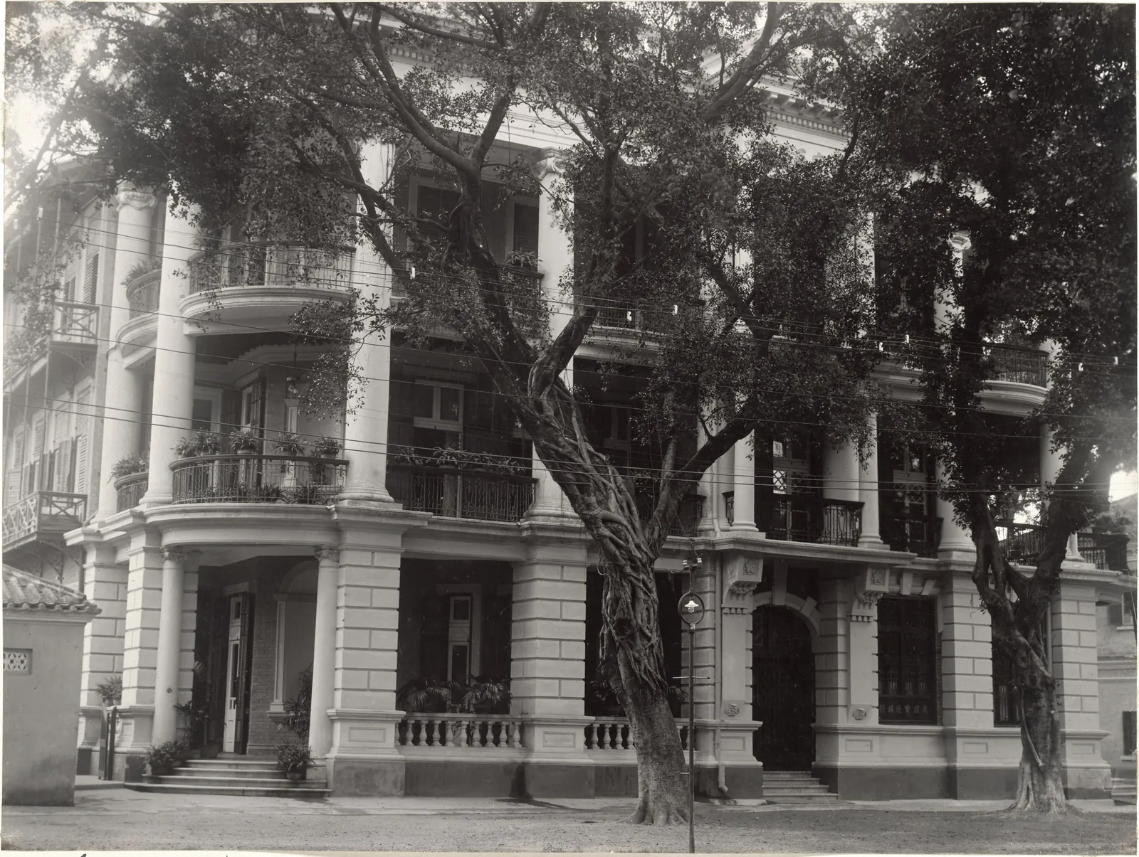 A three-storey corner building with giant columns rising through the upper verandahs, behind a tree.