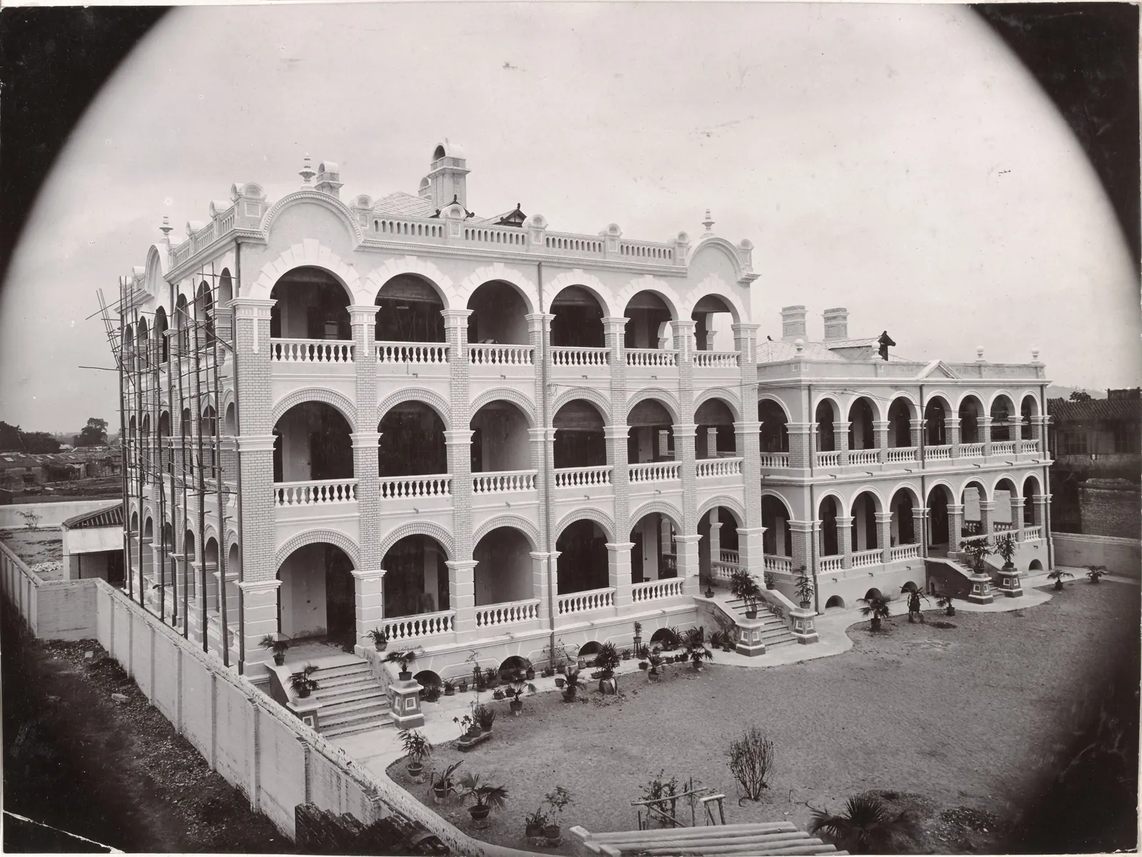 A three-storey arcaded building with balustraded verandahs on a terrace, in a round vignette.